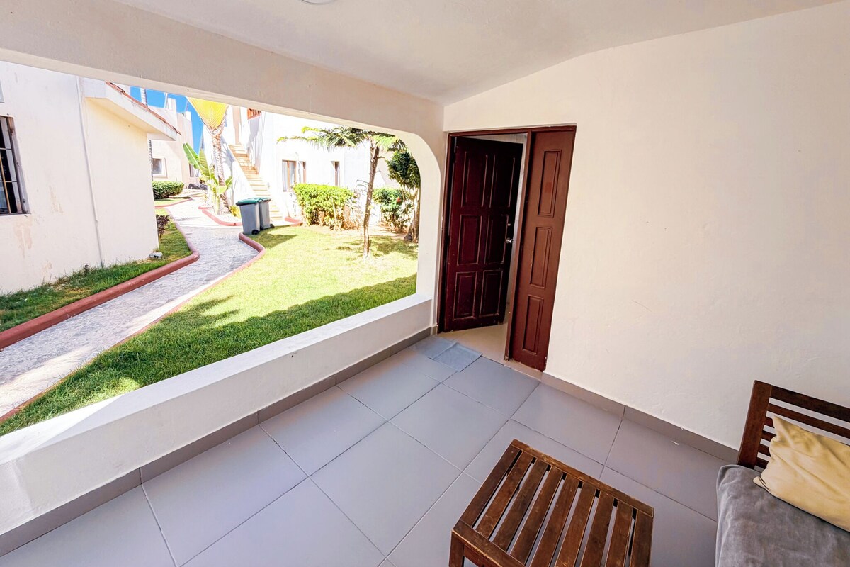 Un balcone con vista su un giardino, una panchina in legno e una porta che dà sull'esterno.
