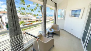 Un balcón con vistas a palmeras y al mar, una silla, una mesita y un tendedero.