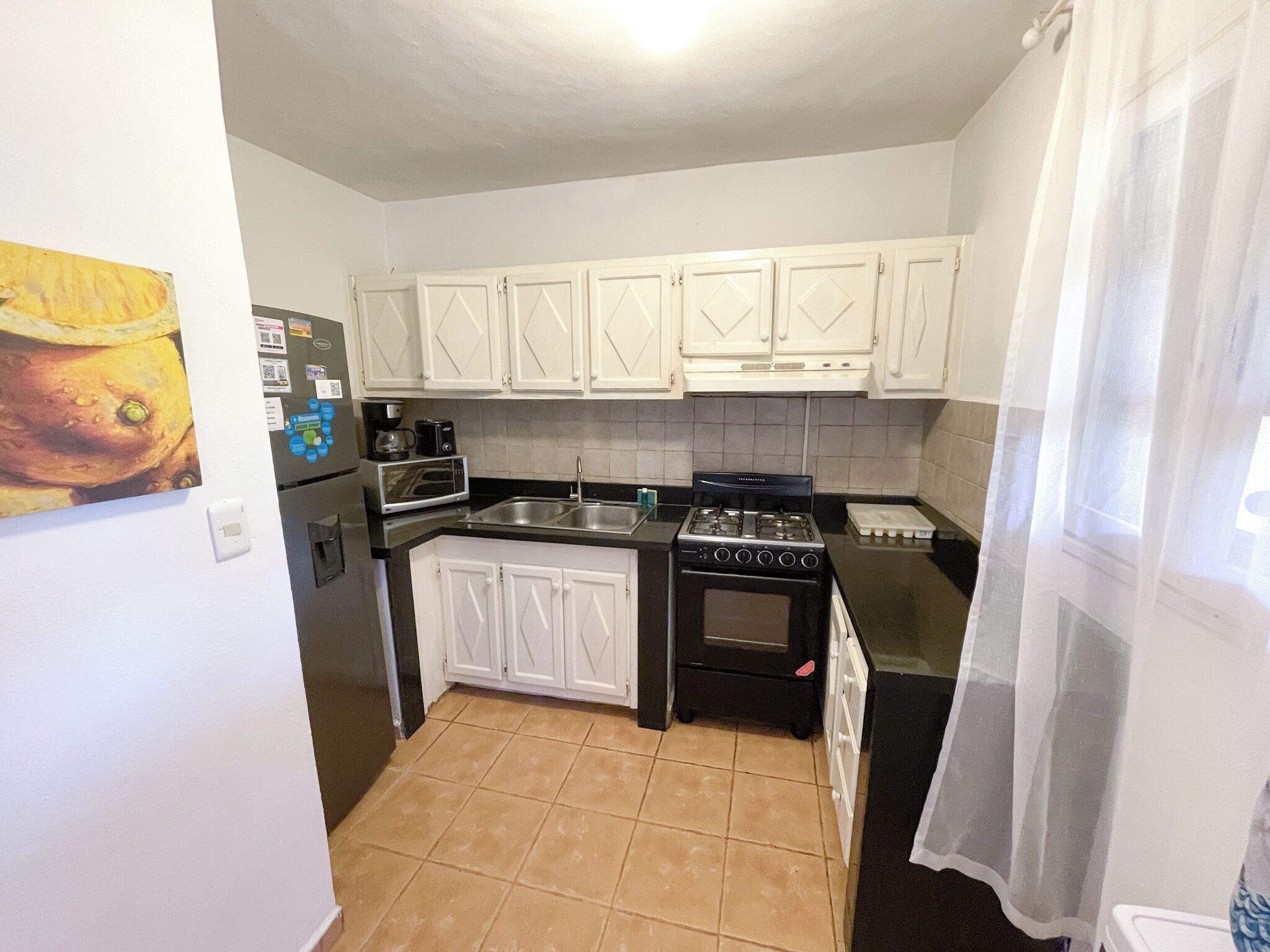 Une cuisine de taille réduite, avec des meubles blancs, une cuisinière, un four à micro-ondes et un réfrigérateur.