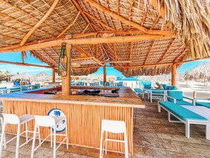 Un bar sulla spiaggia con mobili in legno e un tetto di paglia.