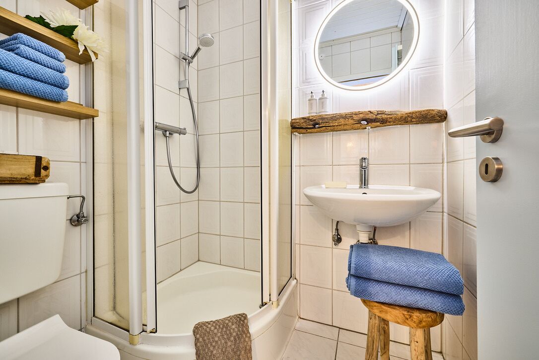 Een badkamer met douche, toilet, wastafel en een houten kruk met handdoeken.