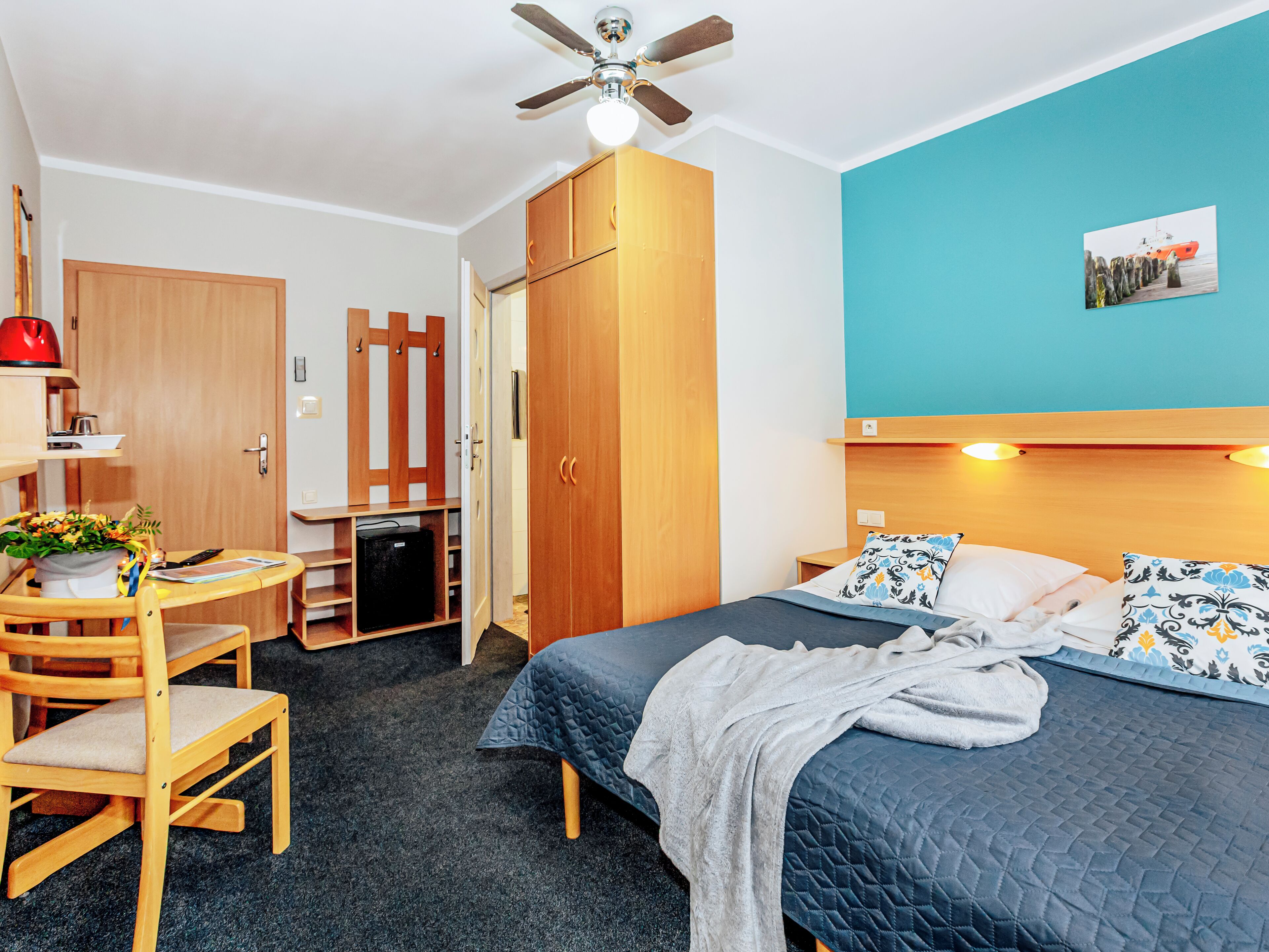 A room with a bed, a desk, a chair, a wardrobe, and a ceiling fan.