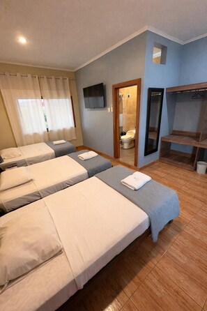 Een hotelkamer met drie bedden, een televisie, een douche en een houten bank.