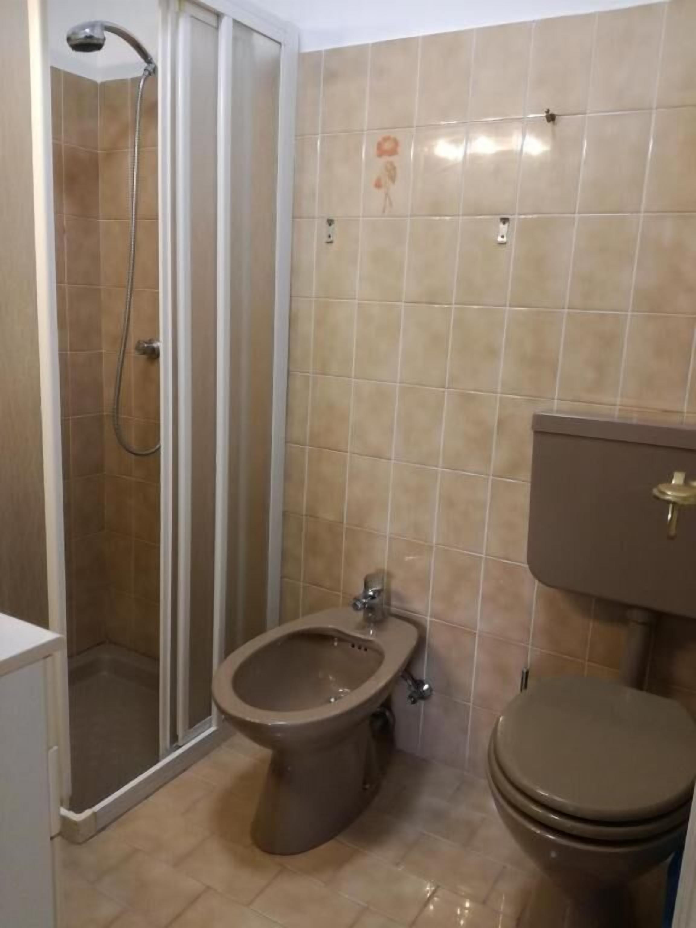 A bathroom with a shower, bidet, toilet, and tiled walls.