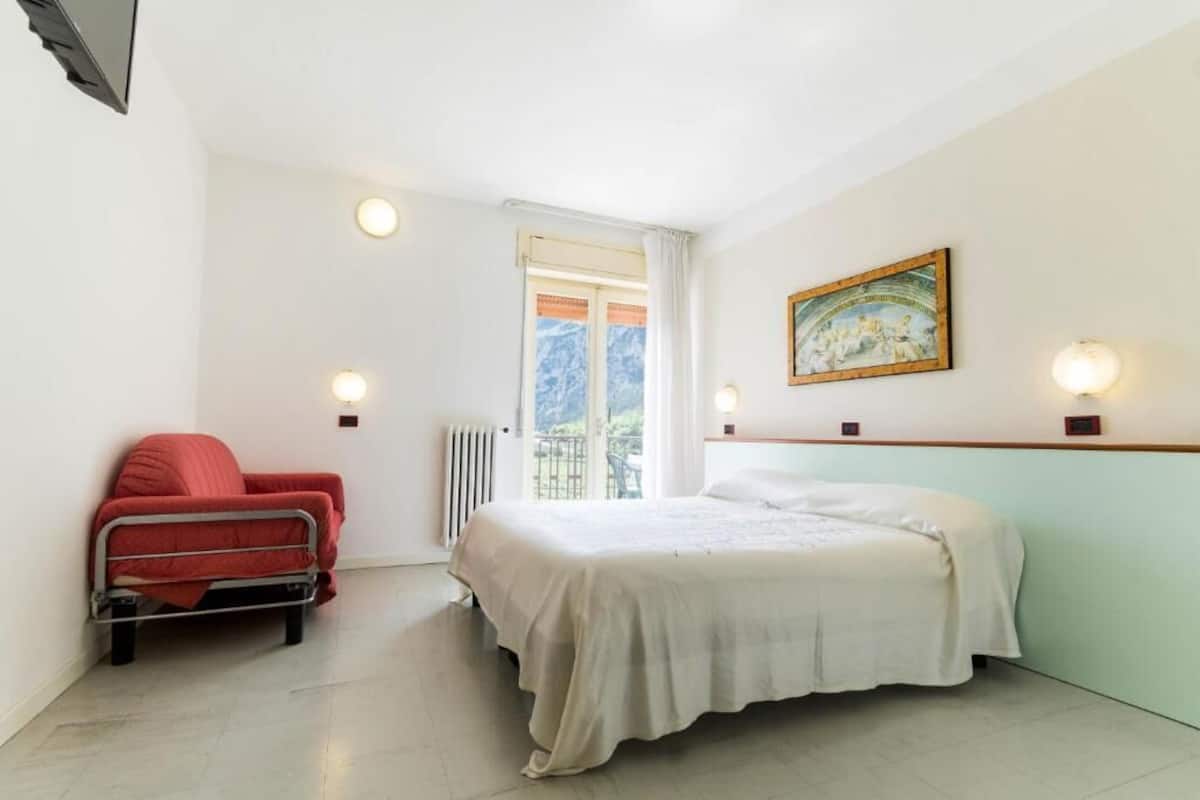 A bedroom with a bed, a chair, a radiator, a window, and a painting on the wall.