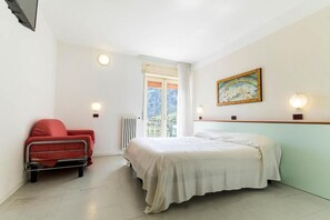 Un dormitorio con una cama, una silla, un radiador, una ventana y un cuadro en la pared.