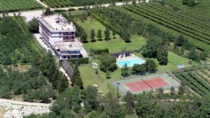 A multi-story building with a rooftop terrace, a swimming pool, and a tennis court surrounded by vineyards. - Aktiv Hotel Eden (Dro)