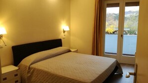 A hotel room with a bed, bedside lamps, a nightstand, and a view of a body of water through a door. - Aktiv Hotel Eden (Dro)