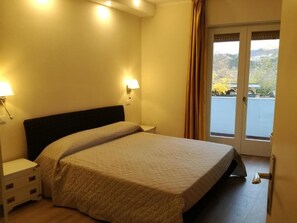 Et hotelværelse med seng, sengeborde, natbord og udsigt til et vandareal gennem en dør.