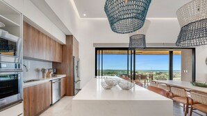 Una cucina moderna con una grande isola, mobili in legno, elettrodomestici in acciaio inossidabile e vista sull'oceano.