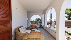 Zona relax esterna coperta con mobili in vimini, una pianta in vaso e vista sugli edifici circostanti.