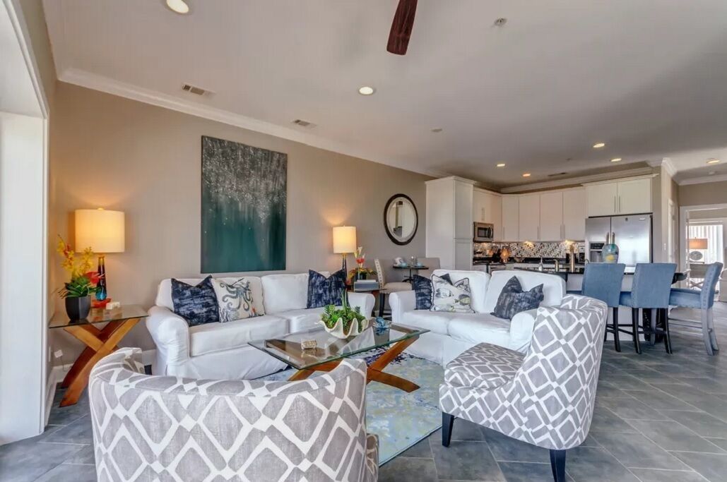 Una sala de estar moderna con un sofá blanco, sillones estampados, una mesa de centro de vidrio y una zona de comedor con una mesa y sillas blancas.