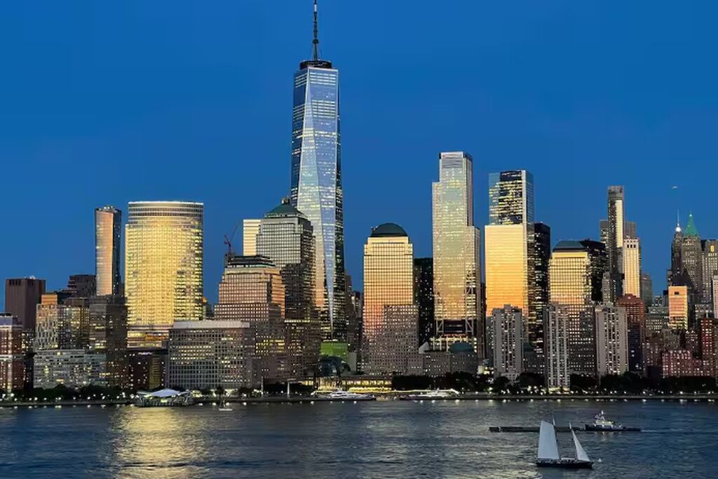 A city skyline with high-rise buildings, a river, and sailboats.