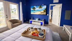 Un dormitorio con cama, televisor en la pared, ventana y una bandeja con comida.
