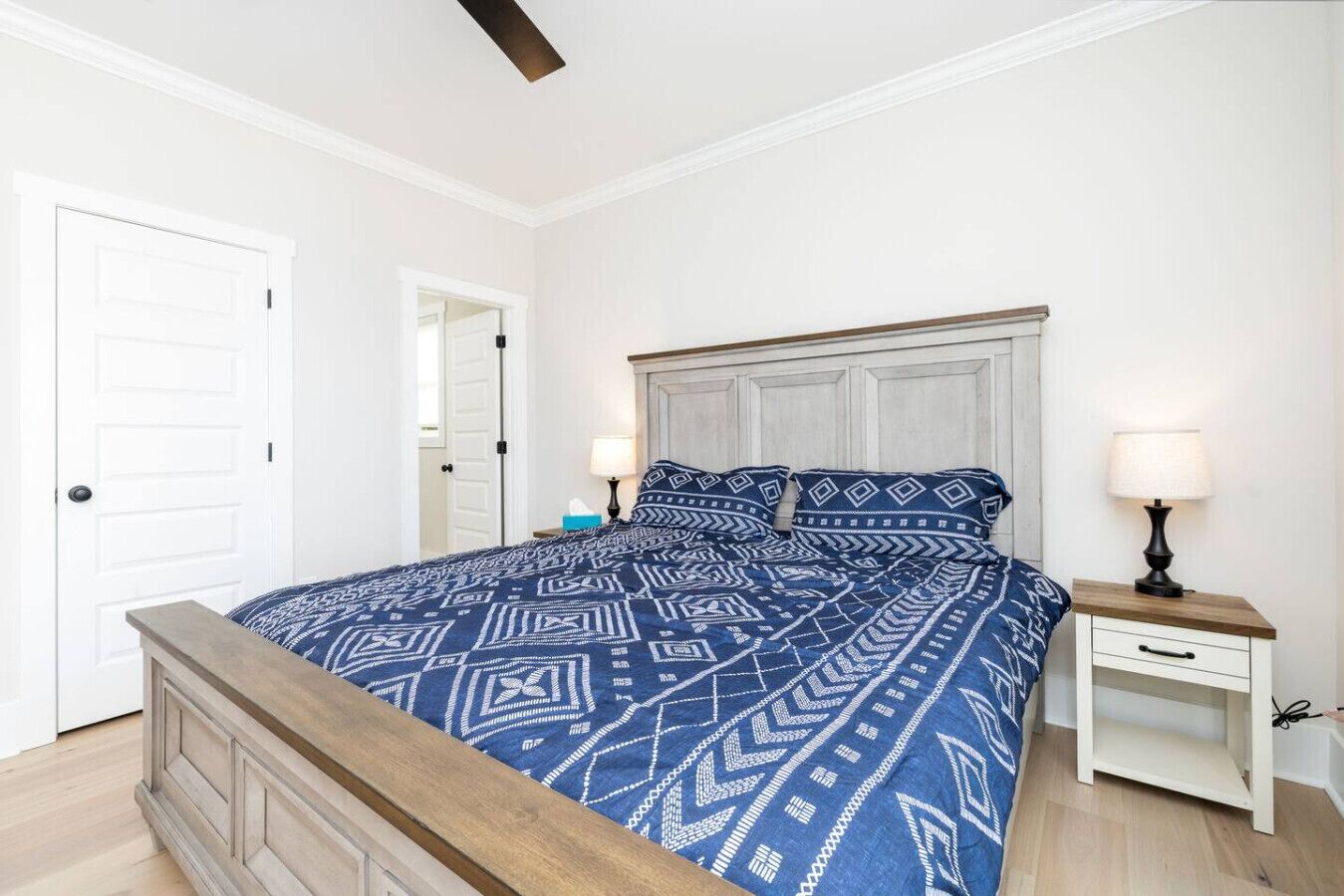 Un dormitorio con cama, mesitas de noche, una puerta y un ventilador de techo.