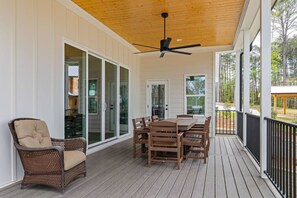 Eine überdachte Terrasse mit Tisch und Stühlen, einem Korbsessel und einem Deckenventilator.