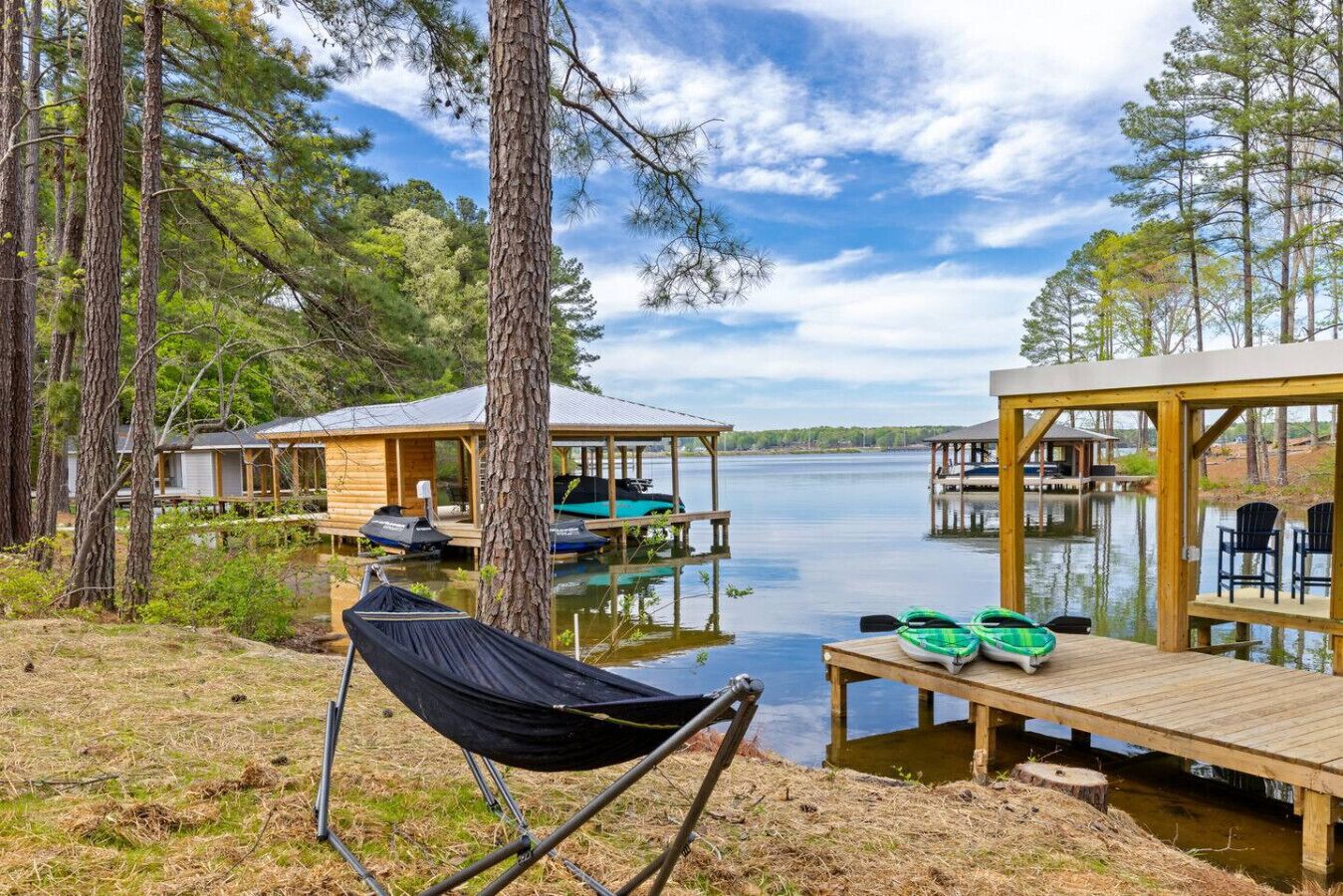 A lakeside cabin with a hammock, kayaks, and a dock extending into the water.