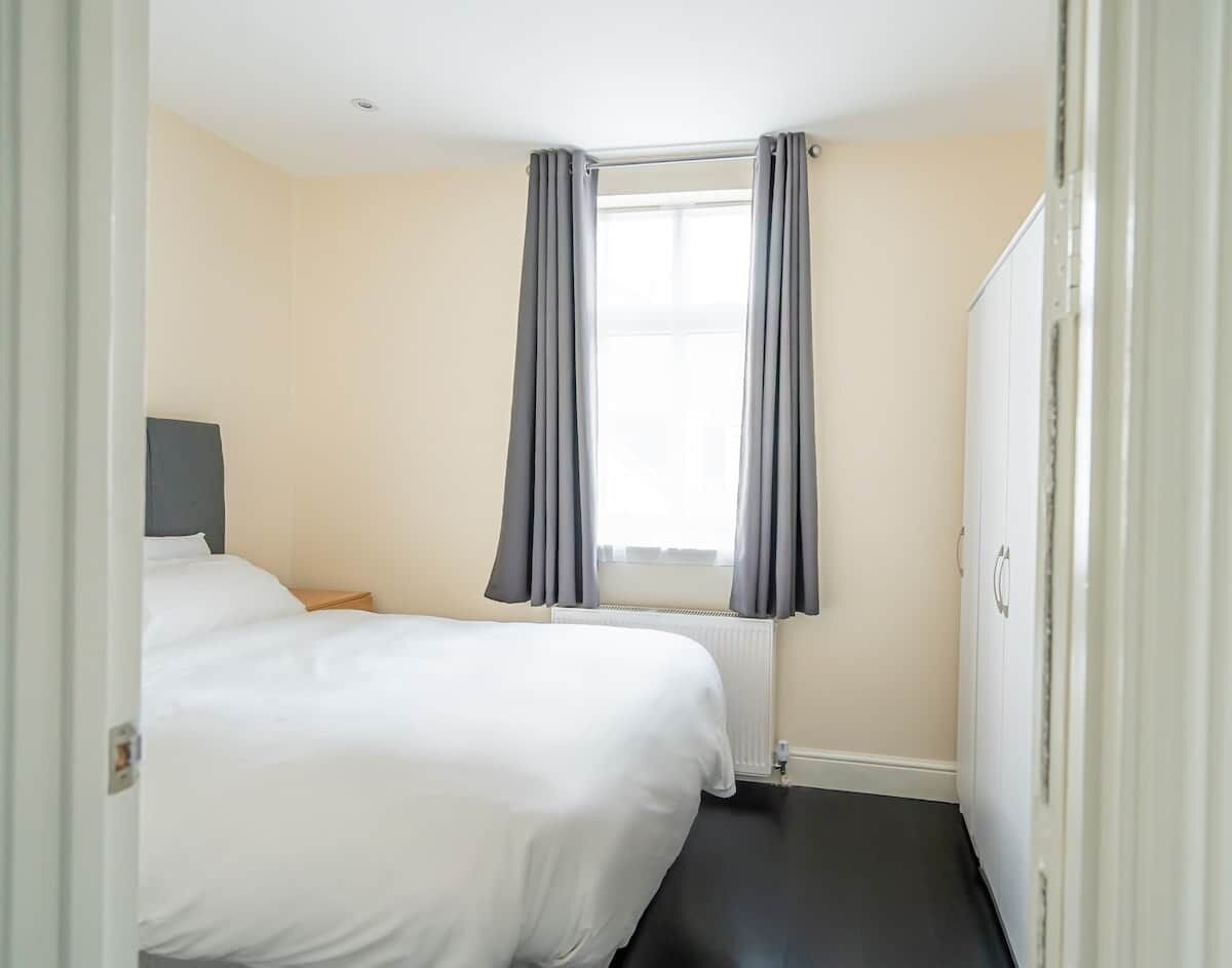 A hotel room with two beds, a window with curtains, a radiator, and a wardrobe.