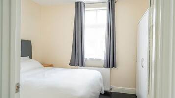 A hotel room with two beds, a window with curtains, a radiator, and a wardrobe.