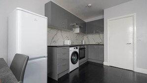 A modern kitchen with a built-in washing machine, grey cabinets, and a white door. - Spacious Flat Near to Barnet Hospital (Barnet)