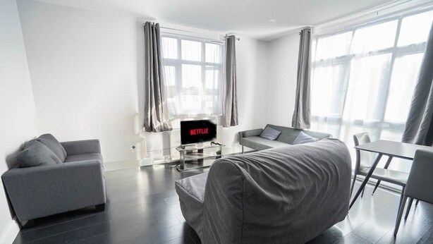 A modern living room with a sofa, a chair, a table, and a TV displaying 'NETFLIX'. - Spacious Flat Near to Barnet Hospital (Barnet)