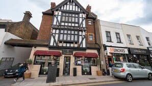 A traditional building with a black and white facade, a sign reading 'The Crown & Anchor,' and adjacent shops including 'Munchies' and 'Uppercutz.' - Spacious Flat Near to Barnet Hospital (Barnet)