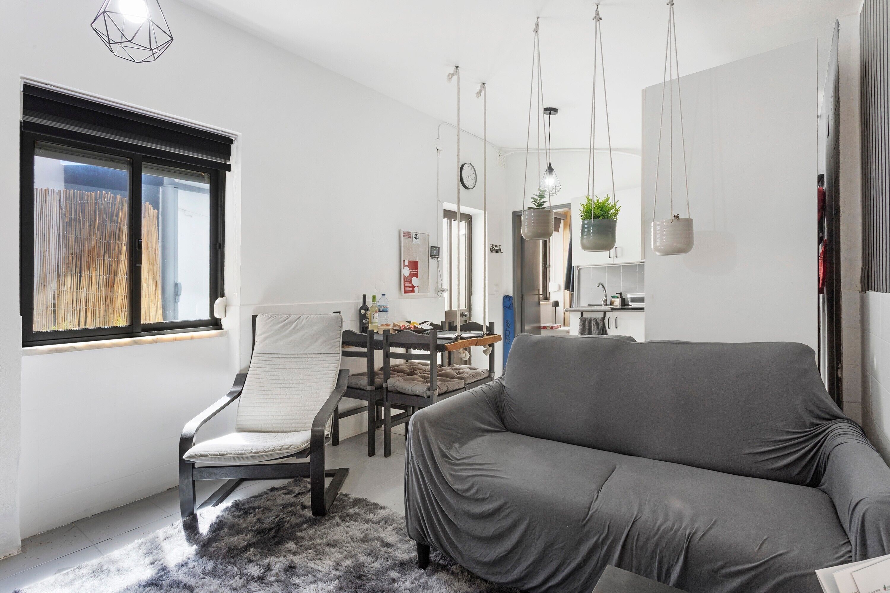 Un salon moderne avec un canapé, un fauteuil, une table à manger et, au fond, un coin cuisine.