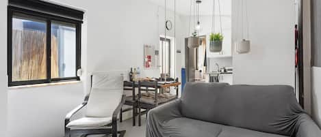 A modern living room with a sofa, a chair, a dining table, and a kitchen area in the background.