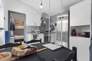 Cocina compacta con electrodomésticos modernos, comedor con mesa y sillas, y una pequeña zona de descanso con cama.