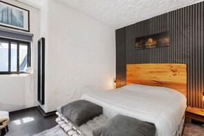 Un dormitorio con una cama grande, una ventana, un cabecero de madera y una obra de arte colgada en la pared.
