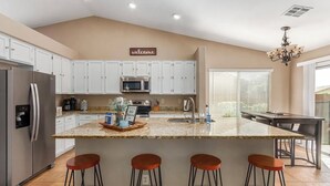 Een moderne keuken met witte kastjes, een centraal eiland met krukken, een magnetron en een koelkast.