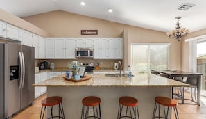 A modern kitchen with white cabinets, a central island with stools, a microwave, and a refrigerator. - Mesa Oasis - Private pool, Patio, Arcades, Family friendly Peaceful neighborhood (Mesa)