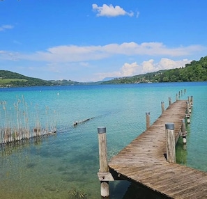 Une jetée en bois s’étendant dans un lac aux eaux limpides, avec une rive visible au loin.