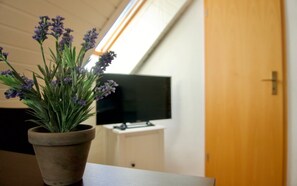 A potted lavender plant on a table in a room with a television and a wooden door.