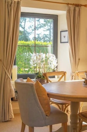 A dining area with a round table, chairs, and a window with curtains.