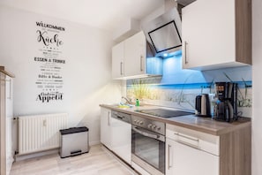Une cuisine moderne avec des meubles blancs, un four en acier inoxydable, un micro-ondes encastré et une machine à café.