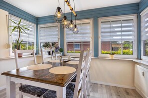 Un espace repas avec une table en bois, des chaises blanches et une vue dégagée grâce à de grandes fenêtres.