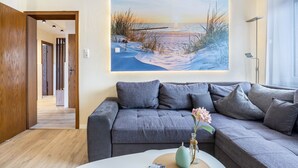Una sala de estar moderna con un sofá gris, un cuadro de una escena de playa y un jarrón con flores sobre una mesa de centro.