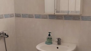 Un bagno con un lavandino su piedistallo, uno specchio sopra, una doccetta e un water.