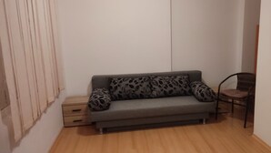Una stanza piccola con un divano grigio, cuscini decorati, un tavolino di legno e una sedia.