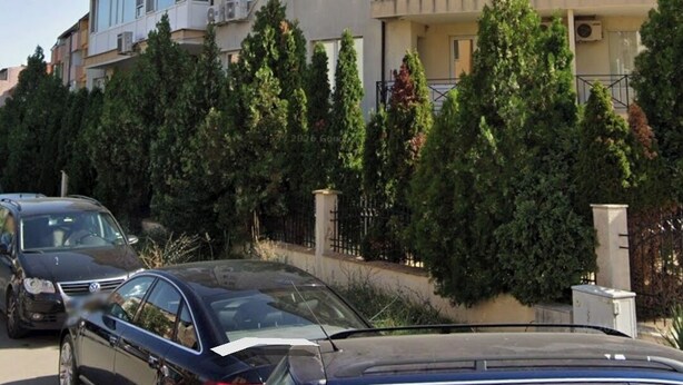 Un edificio residenziale a più piani con balconi, condizionatori e una fila di auto parcheggiate.