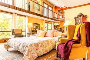 A bedroom with a large bed, a chair, a sofa, a balcony, and a view of trees.