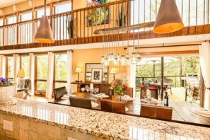 A spacious dining area with a high ceiling, large windows, and a view of the outdoors.