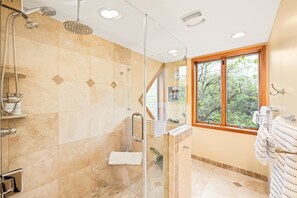 A modern bathroom with a glass-enclosed shower, a wooden-framed window, and a towel rack.