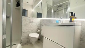 Une salle de bain moderne avec une douche à parois de verre, des toilettes, un lavabo avec un miroir et un mur en marbre.