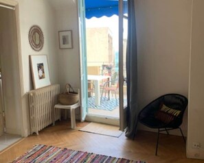 Ein Zimmer mit Holzboden, einem Stuhl, einem Heizkörper, einem gerahmten Bild und Blick auf eine Terrasse.