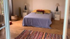 Een slaapkamer met een bed, twee nachtkastjes, een lamp op elk kastje, een kleurrijk vloerkleed en een raam met gordijnen.