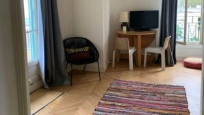 Een kamer met een bureau, twee stoelen, een televisie en een raam met gordijnen.