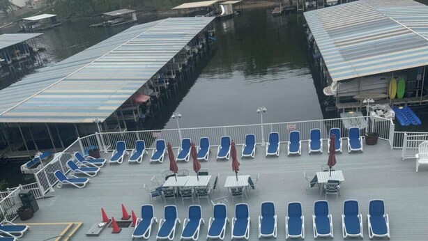A swimming pool with lounge chairs and umbrellas, a dock area with boats, and a building with a covered deck. - Lake front 1-bedroom condo in charming Osage Beach convenient location (Osage Beach)