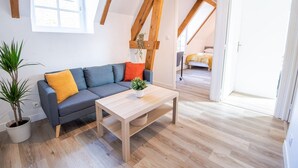Een moderne loftkamer met een houten plafond, een grijze bank met oranje en gele kussens, een houten bijzettafeltje en een potplant.